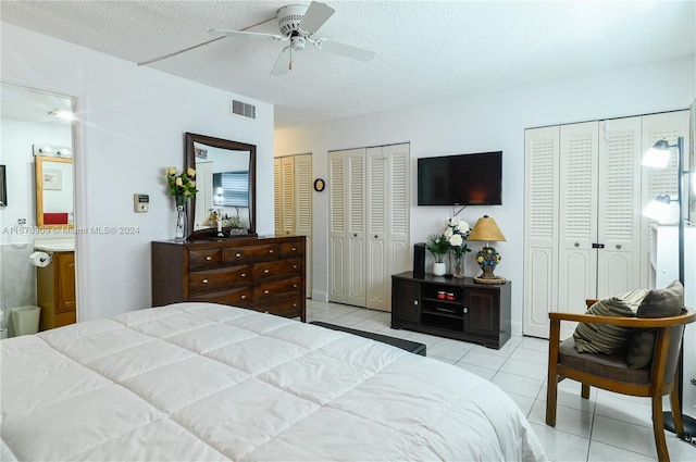 tiled bedroom featuring two closets, ceiling fan, ensuite bathroom, and a textured ceiling