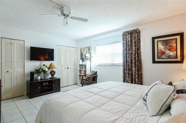 tiled bedroom featuring a textured ceiling, two closets, and ceiling fan