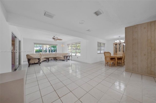 unfurnished living room with ceiling fan with notable chandelier, wood walls, and light tile patterned floors