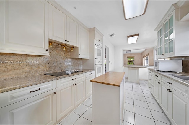 kitchen with wood counters, white cabinets, a kitchen island, backsplash, and light tile patterned floors