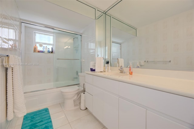 full bathroom featuring tile patterned flooring, combined bath / shower with glass door, toilet, vanity, and tile walls