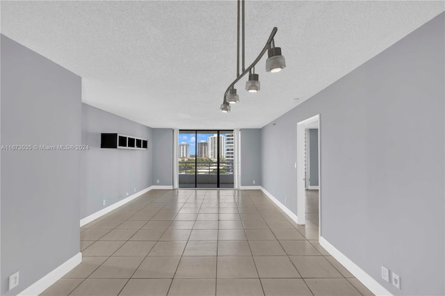 empty room with a textured ceiling, light tile patterned flooring, and expansive windows