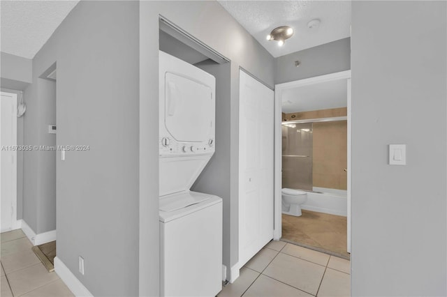 laundry room featuring a textured ceiling, stacked washing maching and dryer, and light tile patterned floors