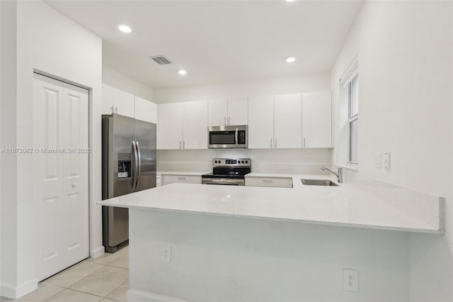 kitchen featuring white cabinets, kitchen peninsula, appliances with stainless steel finishes, and light tile patterned flooring