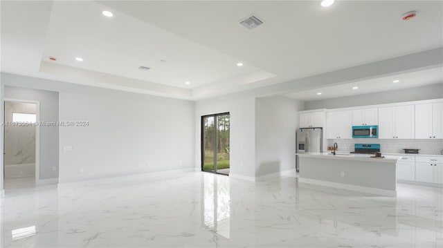 kitchen with appliances with stainless steel finishes, backsplash, a raised ceiling, white cabinets, and a kitchen island with sink