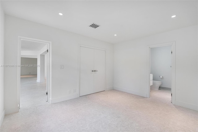 unfurnished bedroom featuring light carpet, ensuite bathroom, and a closet