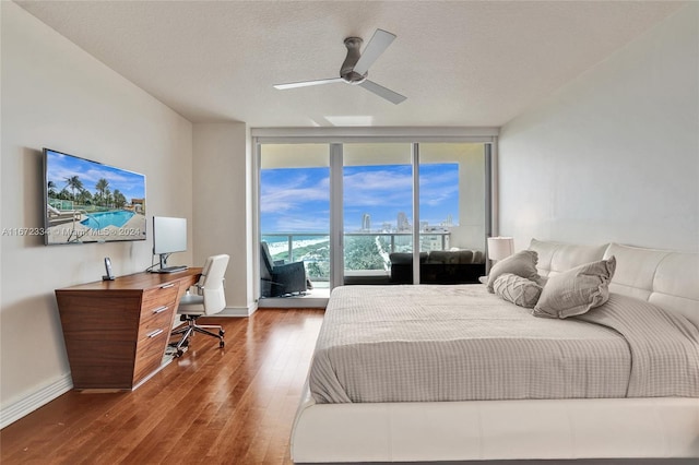 bedroom with ceiling fan, a textured ceiling, access to exterior, wood-type flooring, and floor to ceiling windows