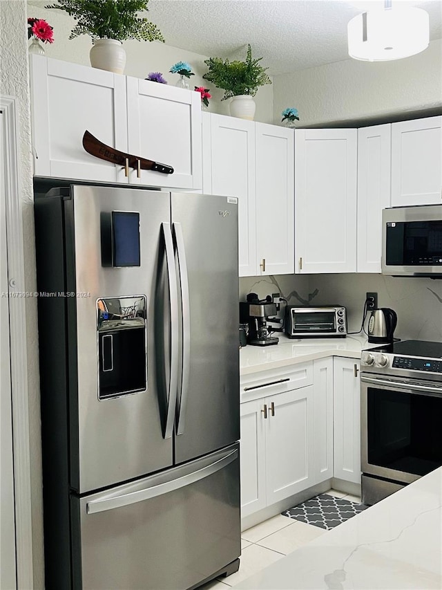 kitchen featuring stainless steel appliances, light tile patterned floors, white cabinets, light stone counters, and a textured ceiling