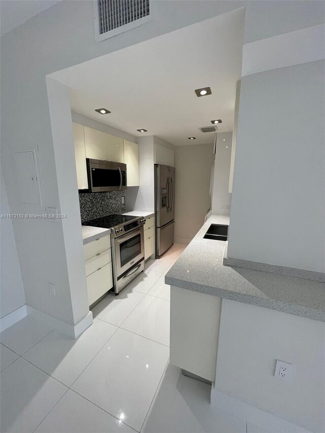 kitchen with light stone counters, white cabinetry, stainless steel appliances, backsplash, and light tile patterned floors