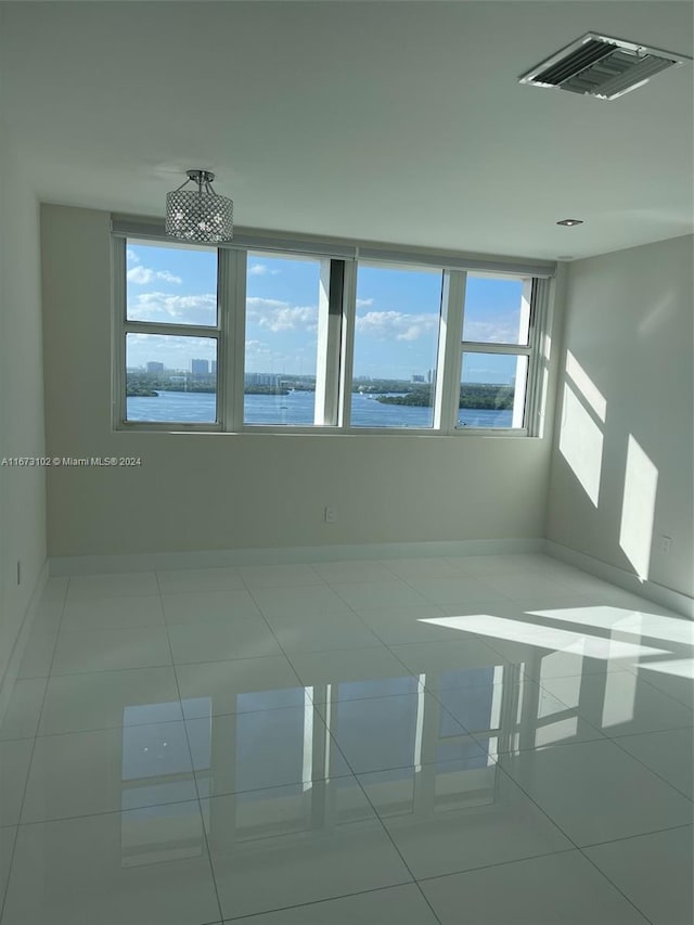 empty room featuring a water view, light tile patterned floors, and a wealth of natural light