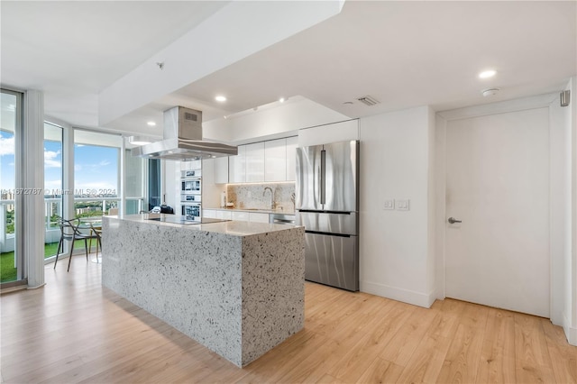 kitchen featuring appliances with stainless steel finishes, white cabinetry, tasteful backsplash, island range hood, and light wood-type flooring