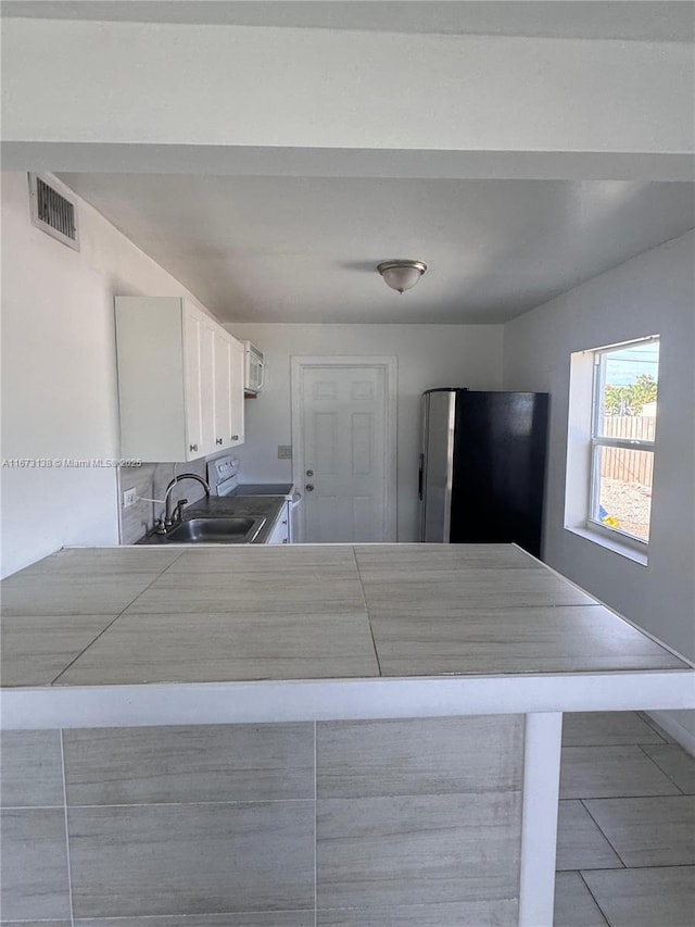 kitchen with stainless steel fridge, white cabinetry, and sink