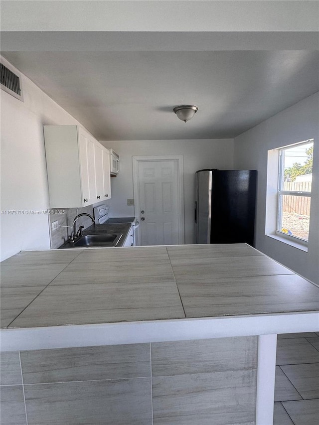 kitchen with tasteful backsplash, sink, white electric range, white cabinetry, and stainless steel refrigerator