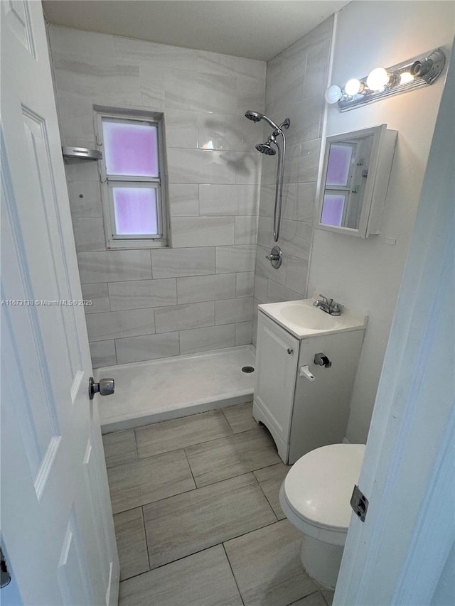 bathroom featuring tiled shower, tile patterned flooring, vanity, and toilet