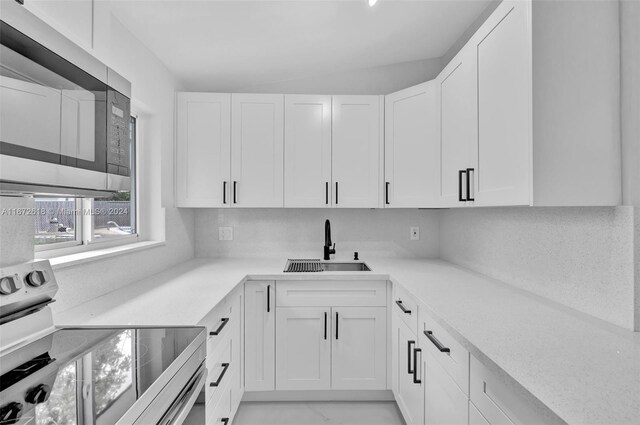 kitchen with sink, backsplash, vaulted ceiling, white cabinets, and range with electric stovetop