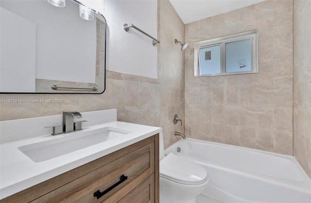 full bathroom featuring vanity, tiled shower / bath, toilet, and tile walls