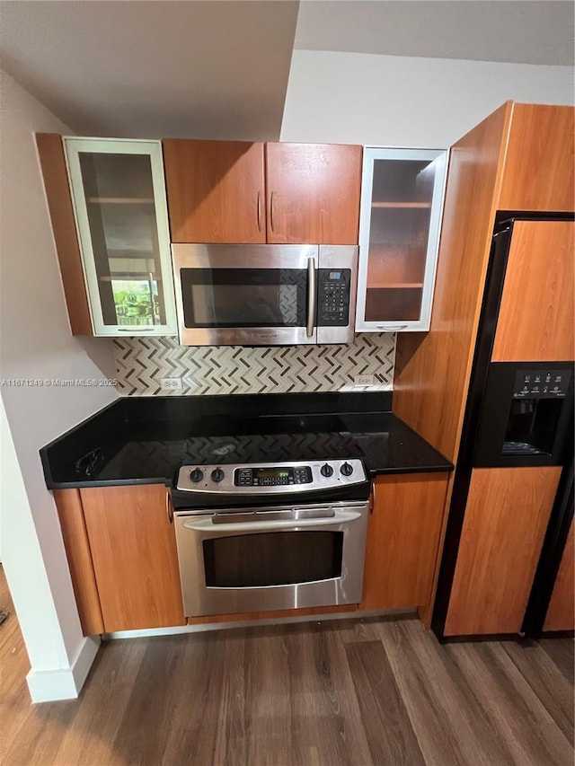 kitchen featuring appliances with stainless steel finishes, dark hardwood / wood-style flooring, dark stone counters, and tasteful backsplash