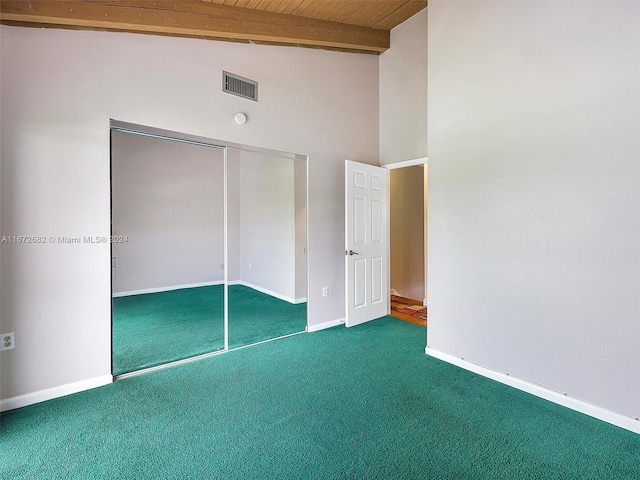 unfurnished bedroom with beam ceiling, a closet, dark carpet, and wooden ceiling