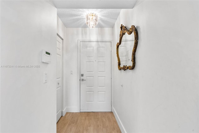 corridor with light wood-type flooring, a textured ceiling, and a chandelier