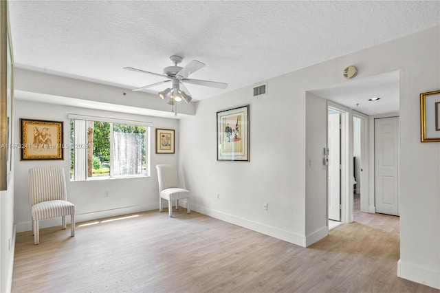 unfurnished room with ceiling fan, a textured ceiling, and light wood-type flooring