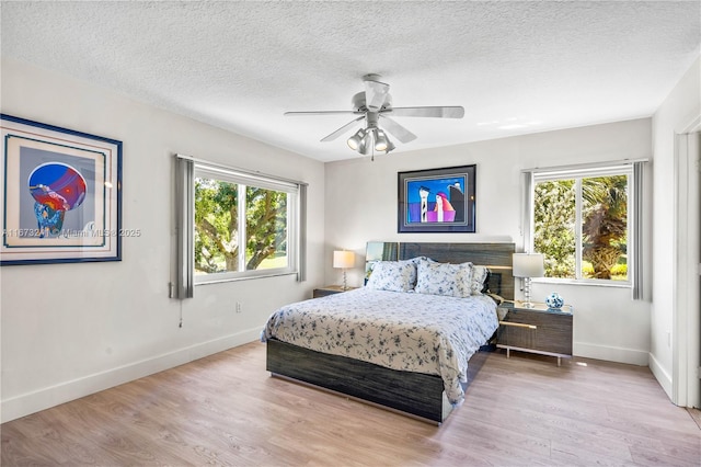 bedroom featuring multiple windows, ceiling fan, light hardwood / wood-style flooring, and a textured ceiling