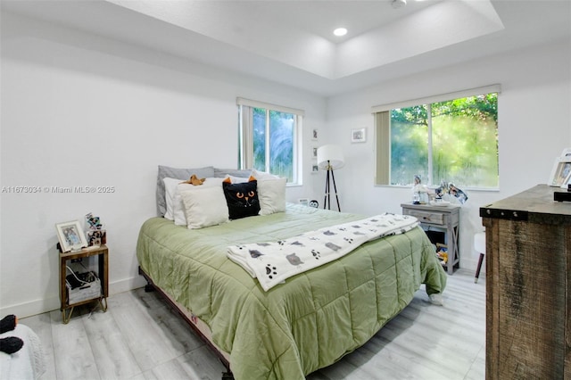 bedroom with a tray ceiling, multiple windows, and light hardwood / wood-style flooring