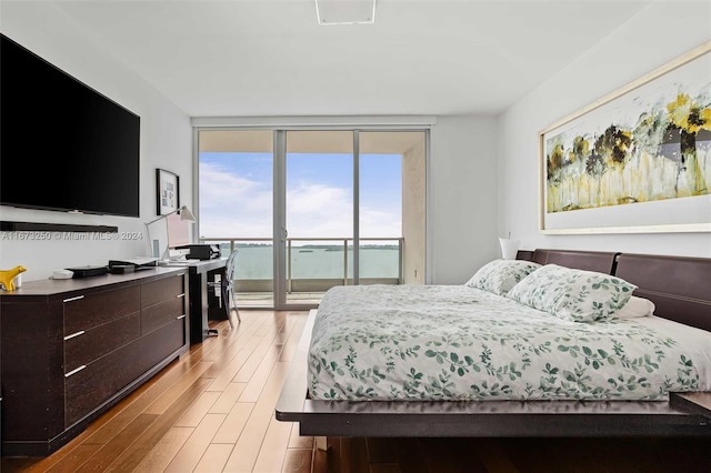 bedroom with light hardwood / wood-style flooring, a water view, a wall of windows, and access to exterior