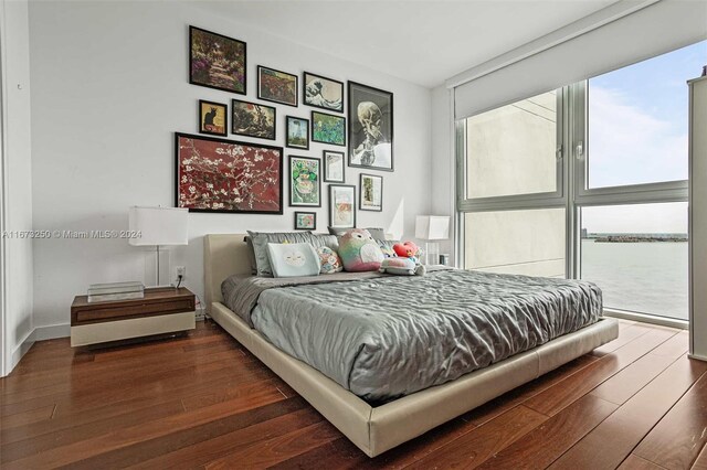 bedroom with dark wood-type flooring and a water view