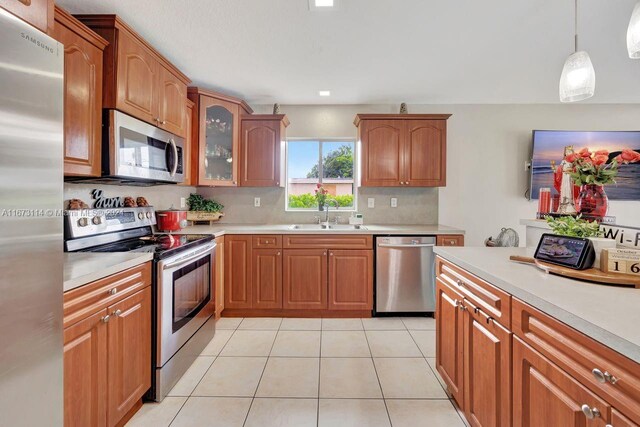 kitchen with hanging light fixtures, backsplash, appliances with stainless steel finishes, light tile patterned floors, and sink