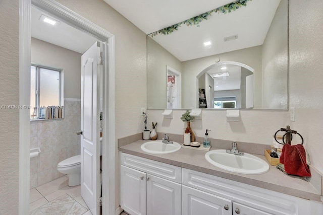 bathroom featuring toilet, vanity, tile patterned floors, and tile walls