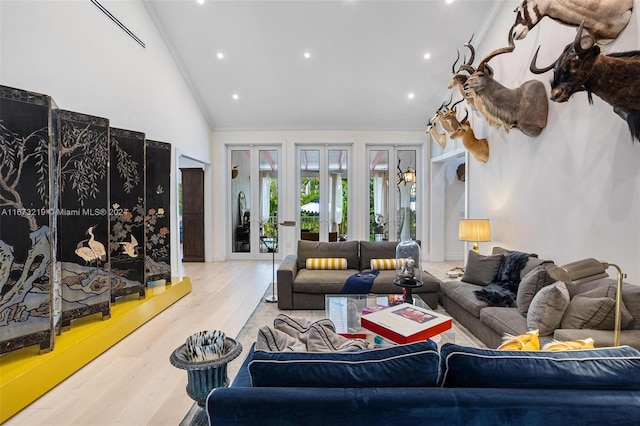 living room featuring lofted ceiling, french doors, ornamental molding, and light hardwood / wood-style flooring