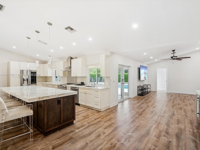 kitchen featuring light stone counters, stainless steel appliances, a spacious island, a breakfast bar area, and vaulted ceiling