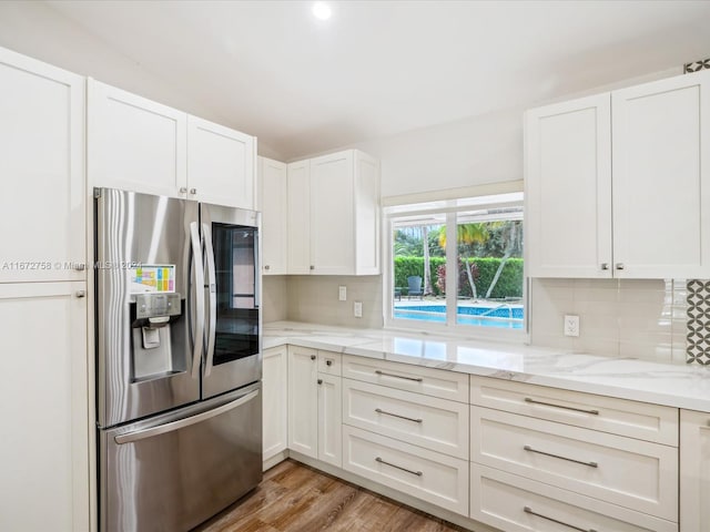 kitchen with stainless steel refrigerator with ice dispenser, light hardwood / wood-style floors, backsplash, and white cabinets