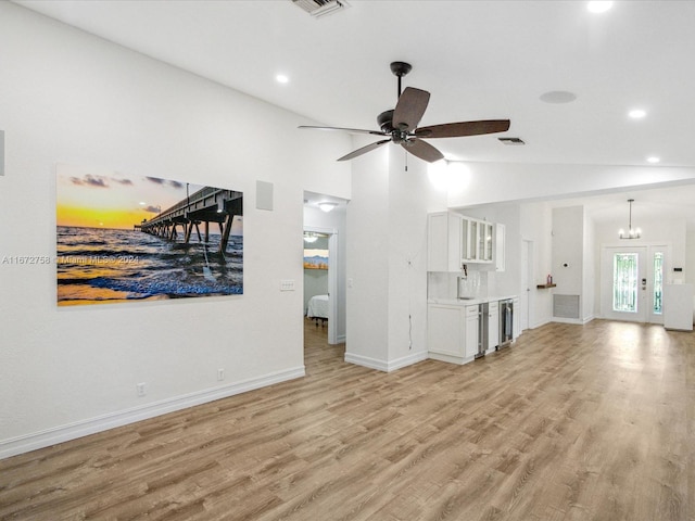 unfurnished living room with ceiling fan with notable chandelier, vaulted ceiling, beverage cooler, and light hardwood / wood-style flooring