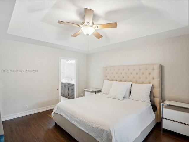 bedroom featuring a tray ceiling, ceiling fan, ensuite bathroom, and dark hardwood / wood-style flooring