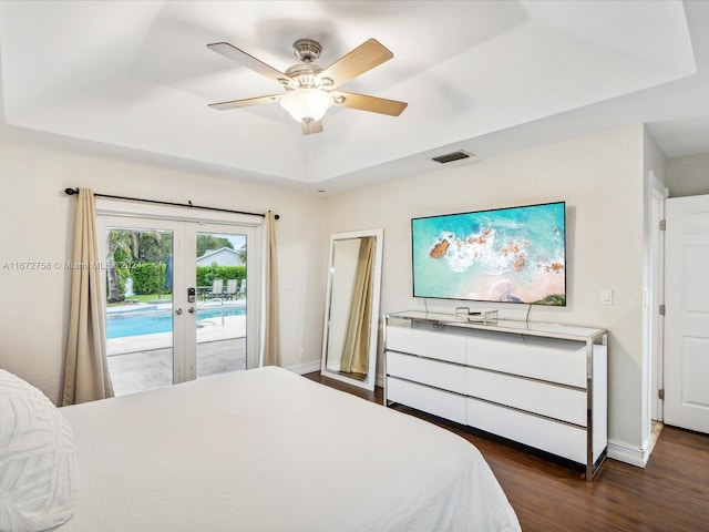 bedroom featuring a tray ceiling, access to exterior, dark wood-type flooring, ceiling fan, and french doors