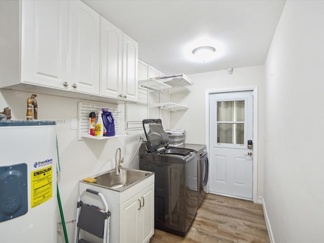 washroom featuring water heater, washing machine and dryer, light wood-type flooring, cabinets, and sink