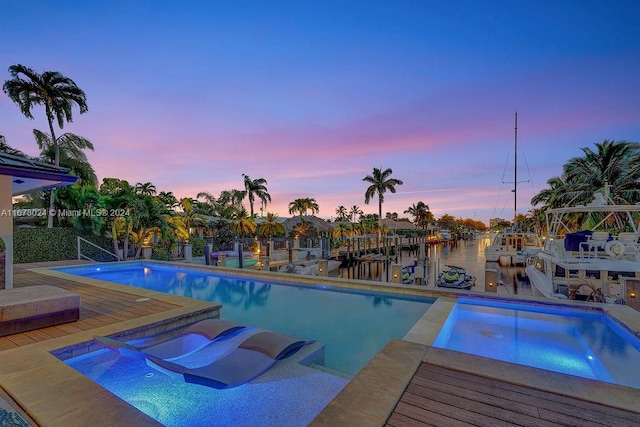 pool at dusk featuring a water view, a patio, and an in ground hot tub