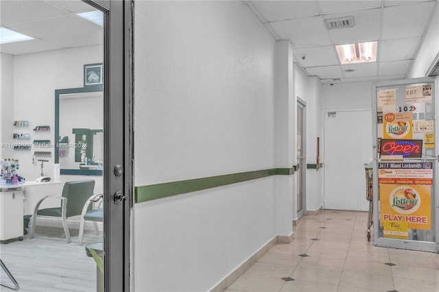 hall featuring a drop ceiling and light tile patterned floors