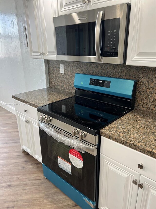 kitchen with white cabinets, appliances with stainless steel finishes, light hardwood / wood-style floors, and dark stone counters