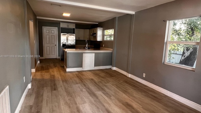 kitchen with gray cabinetry, sink, kitchen peninsula, hardwood / wood-style floors, and stainless steel refrigerator with ice dispenser