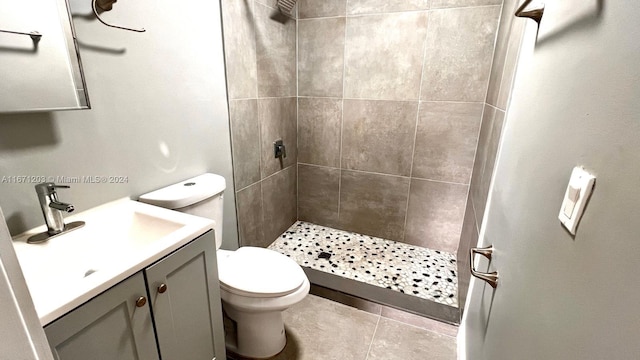 bathroom with toilet, vanity, a tile shower, and tile patterned floors