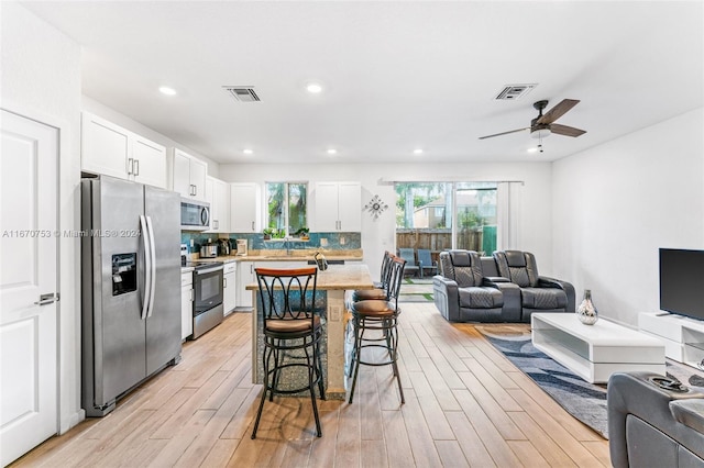 kitchen with ceiling fan, white cabinets, light hardwood / wood-style flooring, stainless steel appliances, and a breakfast bar