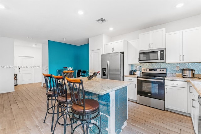 kitchen with stainless steel appliances, light wood-type flooring, white cabinetry, and a kitchen island