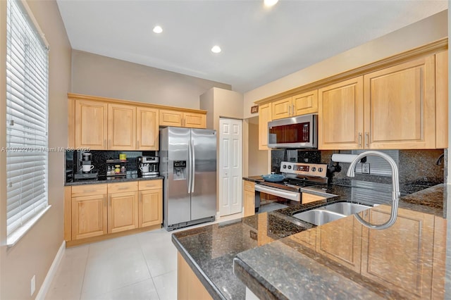 kitchen featuring dark stone countertops, light brown cabinetry, appliances with stainless steel finishes, and tasteful backsplash