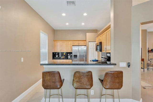 kitchen featuring kitchen peninsula, a breakfast bar area, light tile patterned floors, and appliances with stainless steel finishes