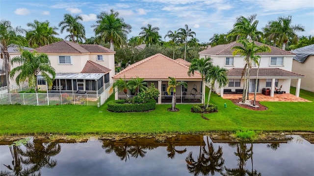 rear view of house with a sunroom, a lawn, and a water view