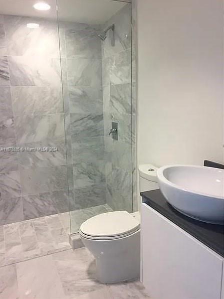 bathroom with a tile shower, toilet, and vanity