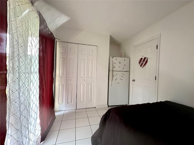 bedroom featuring freestanding refrigerator, a closet, and light tile patterned floors