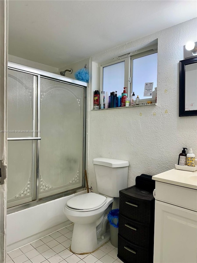 full bath featuring bath / shower combo with glass door, a textured wall, toilet, vanity, and tile patterned floors